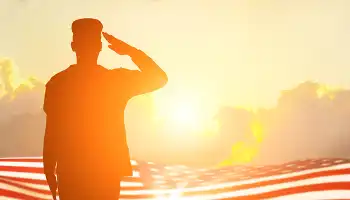 Veteran saluting, American flag in background, at sunset