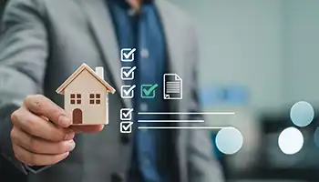 Person holding wooden house model with property checklist overlay.