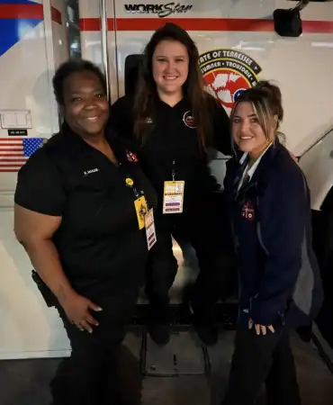 3 woman stand in front of mobile command vehicle