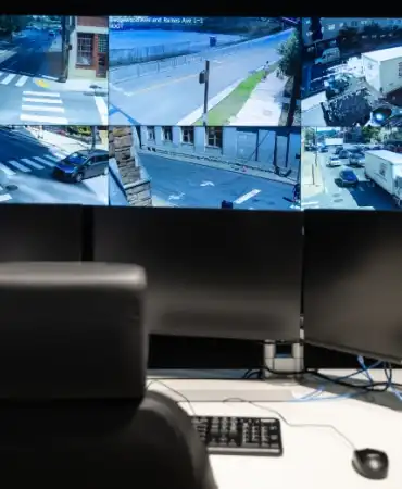 Interior view of the Traffic Management Center showing multiple large monitors displaying traffic camera feeds with workstations for staff to monitor traffic conditions