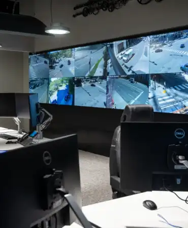 Interior view of the Traffic Management Center showing multiple large monitors displaying traffic camera feeds with workstations for staff to monitor traffic conditions