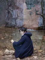 A women wearing a navy colored jacket kneeling on a rocky river bank